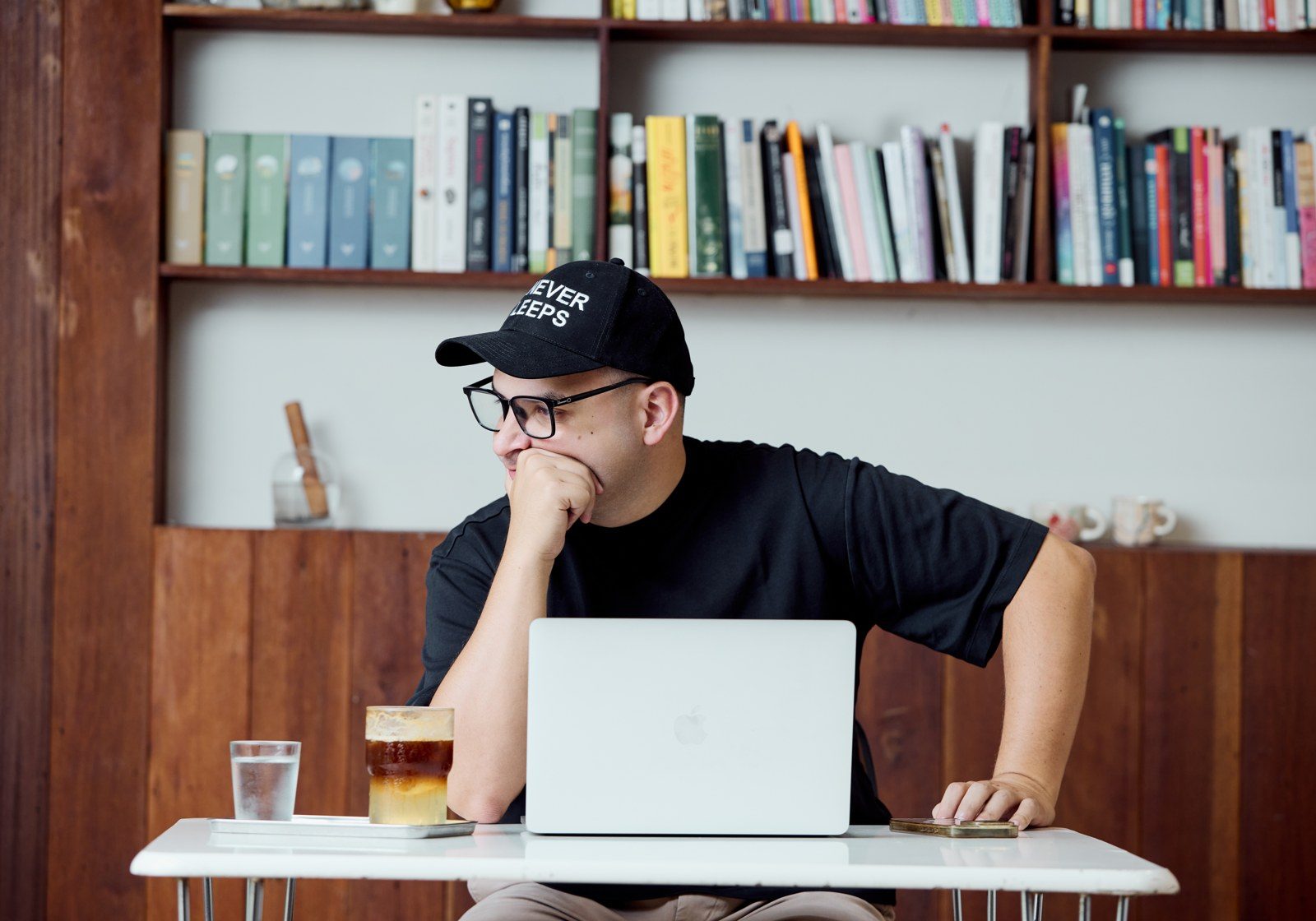 Ruben working on a laptop in a cafe, AI Never Sleeps cap